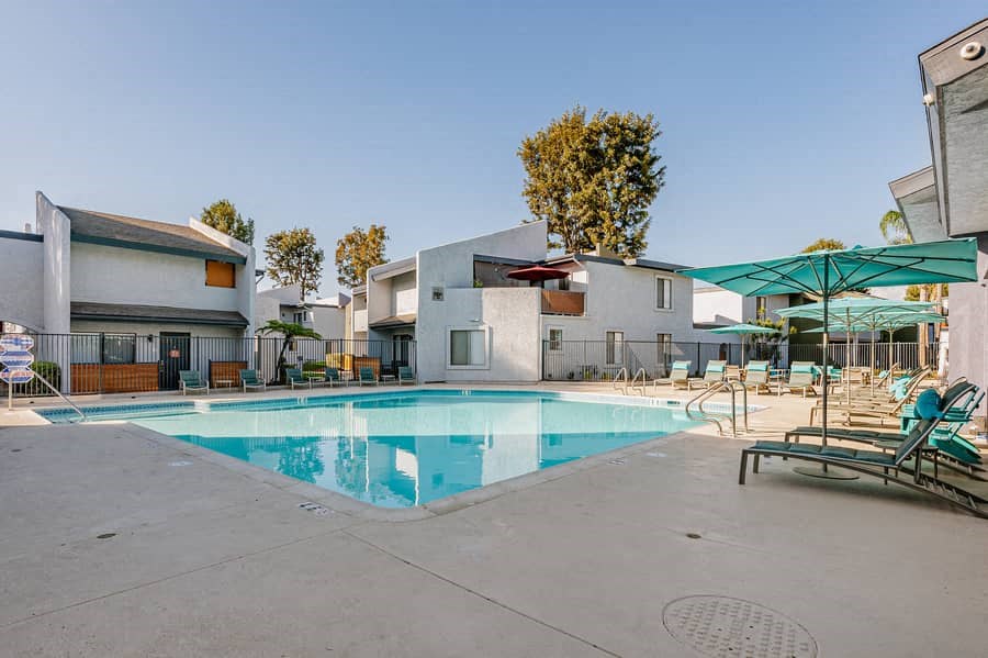 a swimming pool with chairs and umbrellas at an apartment complex