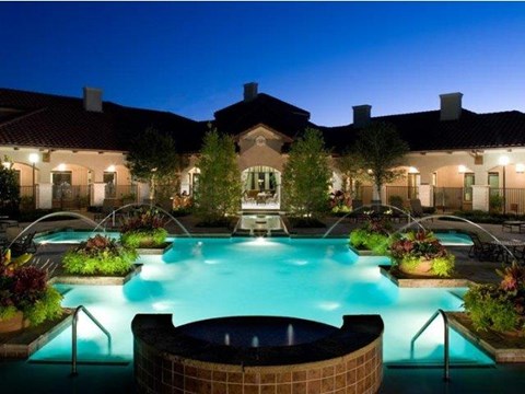 A large outdoor swimming pool surrounded by a brick border and a hot tub in the middle.