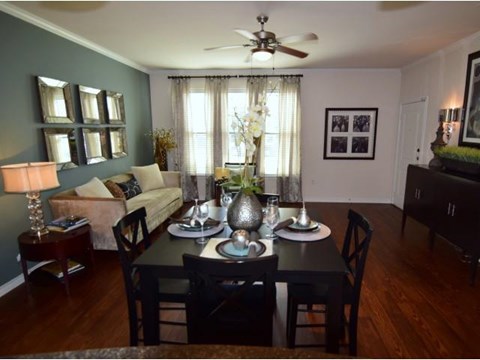 A dining room with a table set for two and a couch with a lamp and vase on it.
