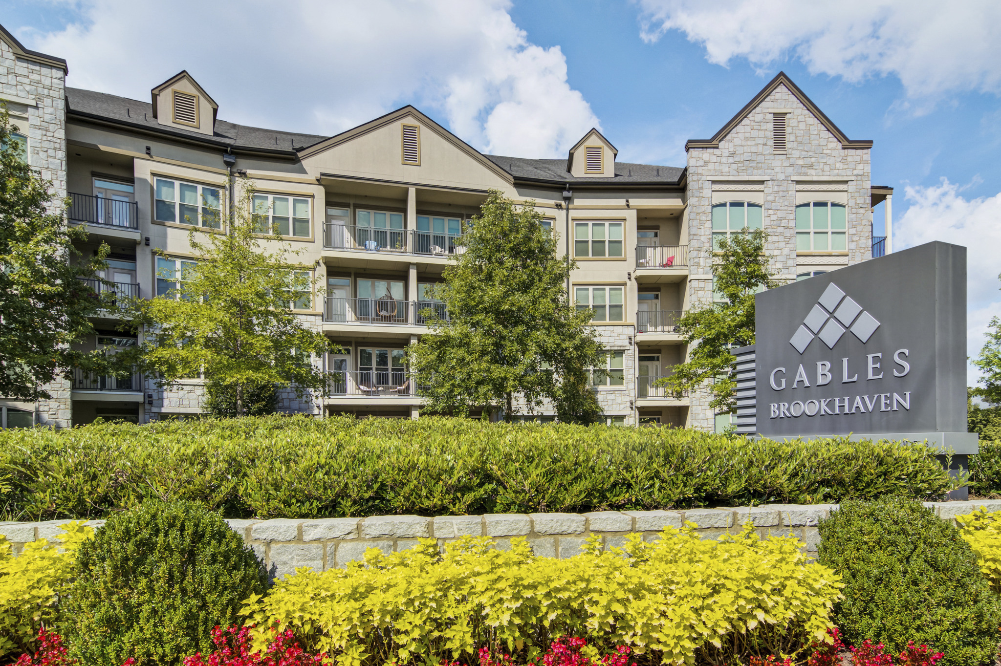 an apartment building with a sign in front of a stone retaining wall and a garden