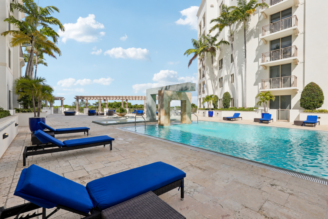 A pool area with blue lounge chairs and a white building in the background.