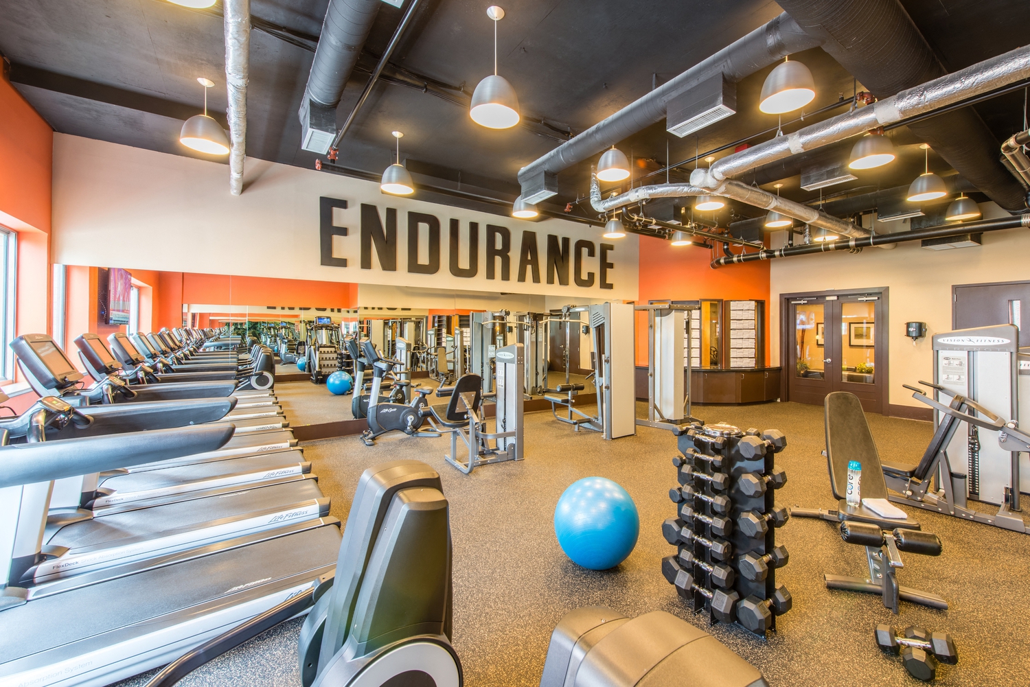 a gym with weights and cardio machines and a sign on the ceiling that reads endurance