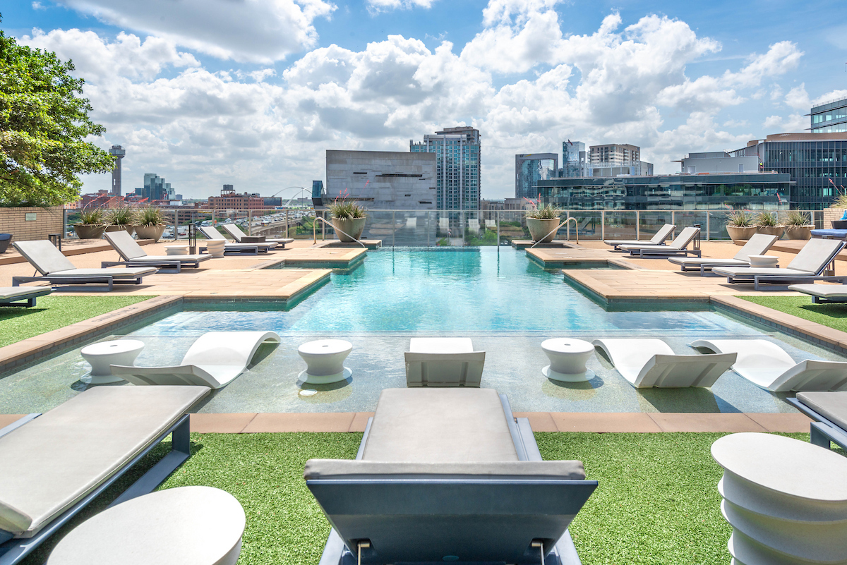 A large outdoor swimming pool surrounded by lounge chairs and a city skyline in the background.
