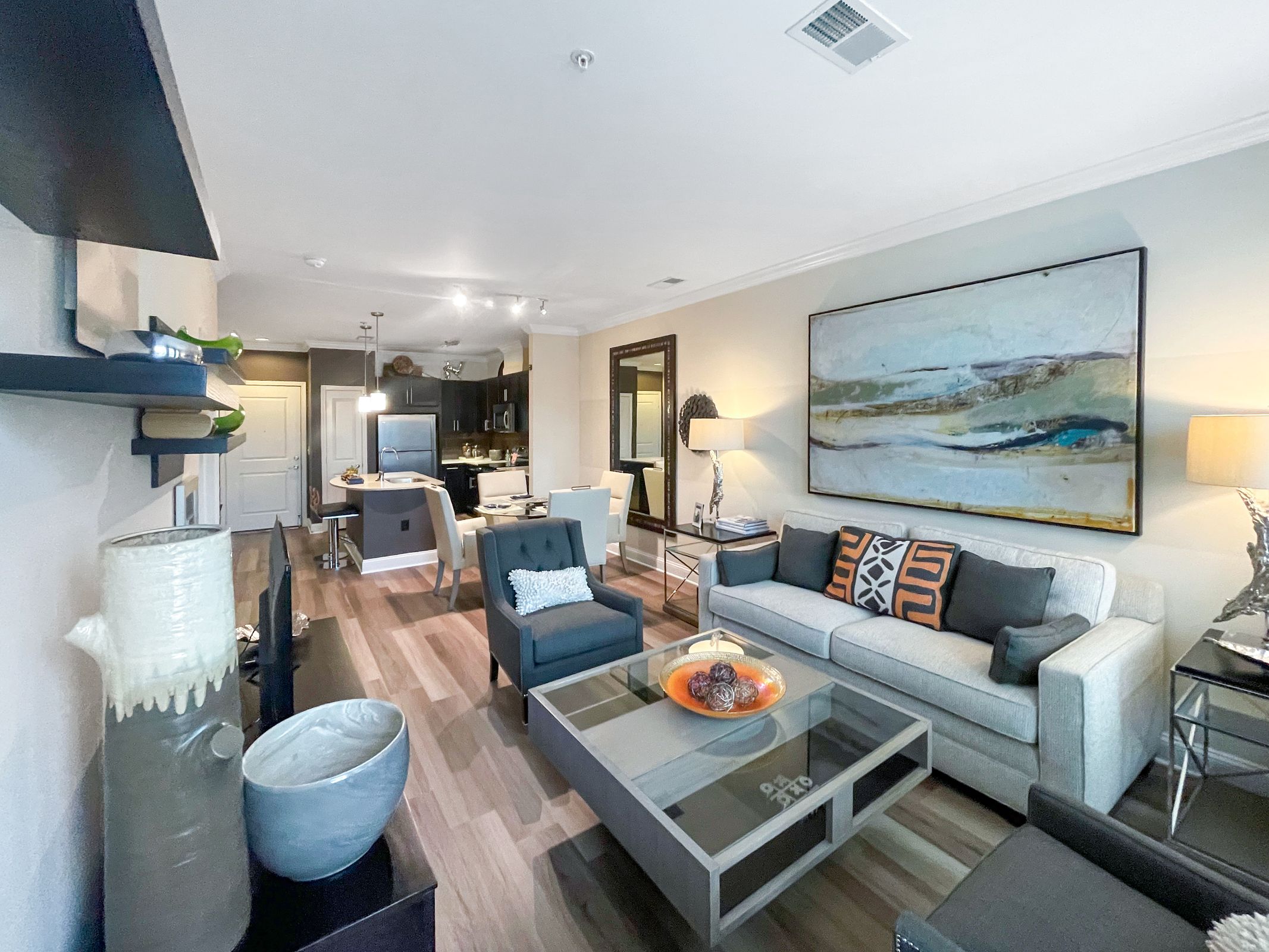 A modern living room with a grey couch and a painting on the wall.