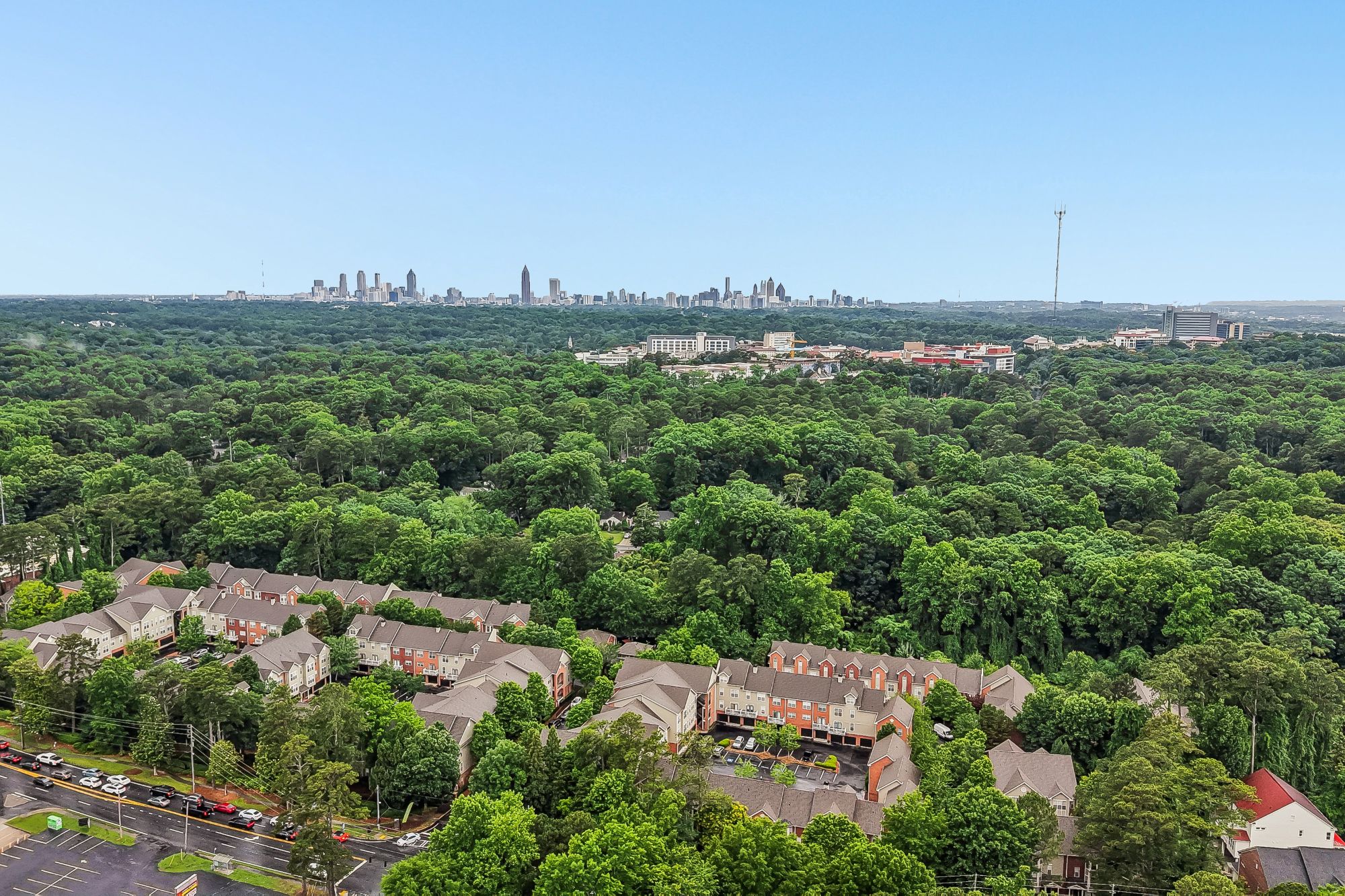 A bird's eye view of a residential area surrounded by trees with a city skyline in the distance.