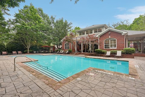 A pool surrounded by a brick patio and a house in the background.