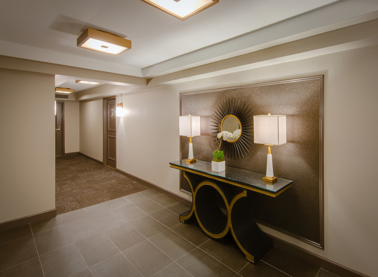 a hallway with a table with two lamps and a mirror