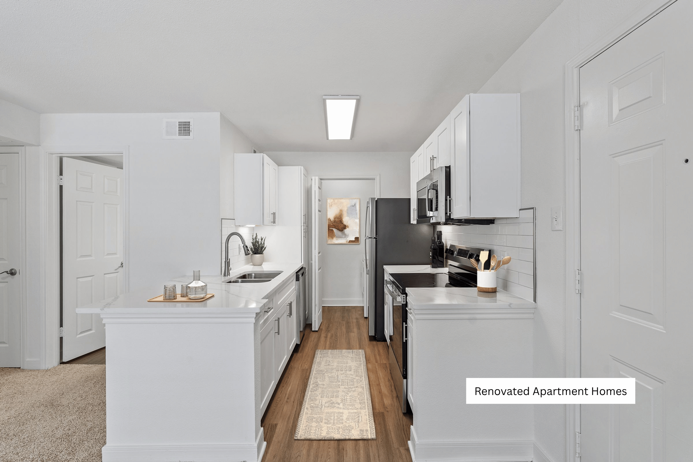 A renovated apartment kitchen with white cabinets and appliances.