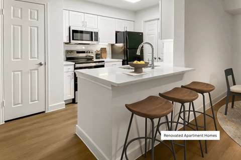 A kitchen with white cabinets and a white island with three stools.