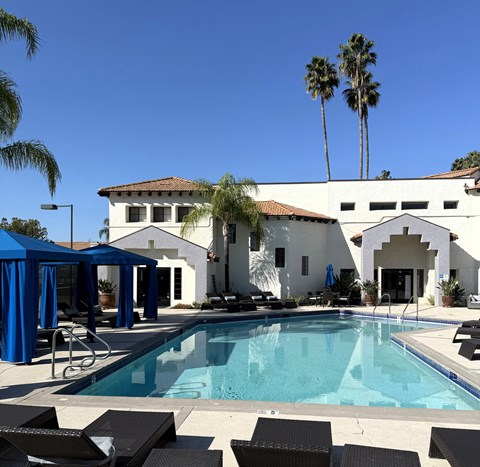 A pool with lounge chairs and a white building with a red roof.