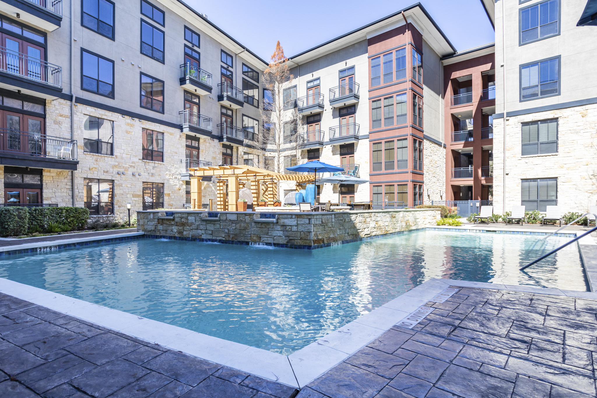 an outdoor pool with a stone wall and a waterfall in front of an apartment building