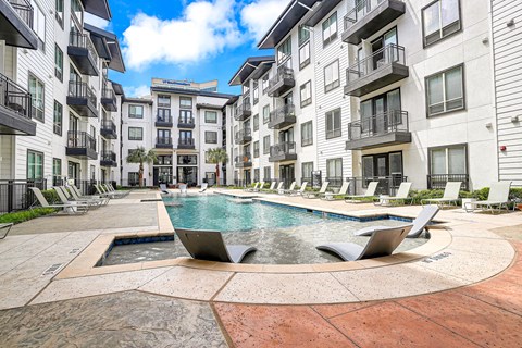 A large swimming pool surrounded by lounge chairs and buildings.