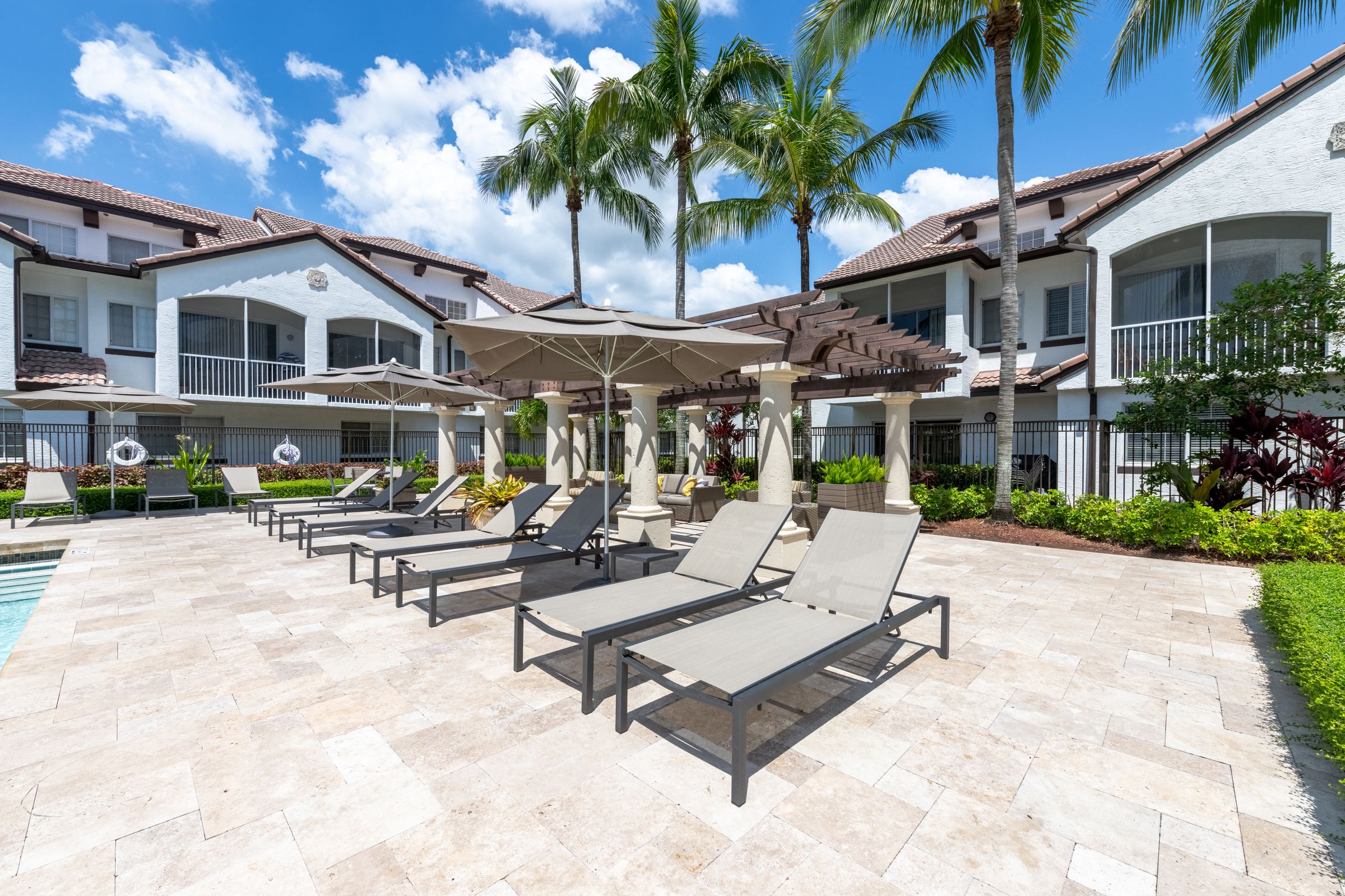 a patio with lounge chairs and umbrellas in front of some houses