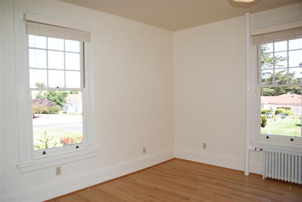 an empty room with two windows and a wooden floor