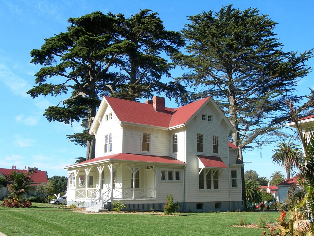 a white house with a red roof next to a tree