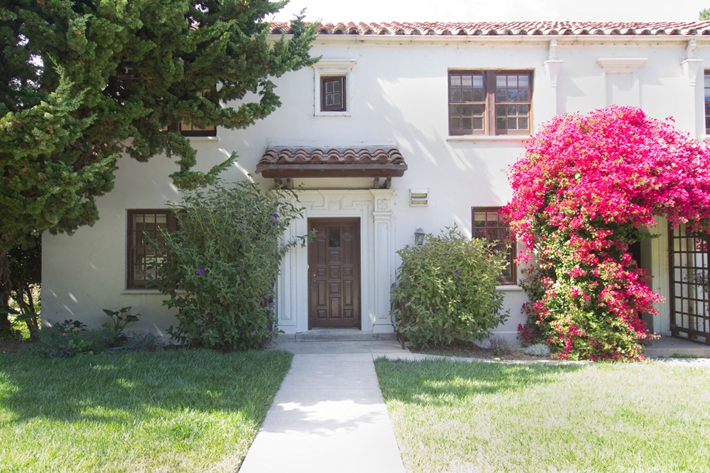 the front of a white house with a walkway and trees and flowers