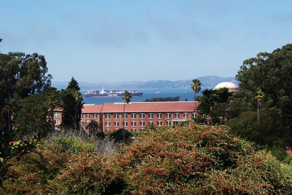 a large building with trees in the foreground and a body of water in the background