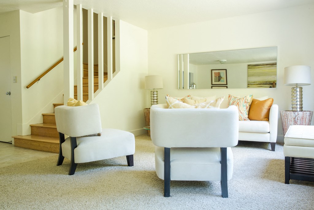 a living room with two white chairs and a staircase