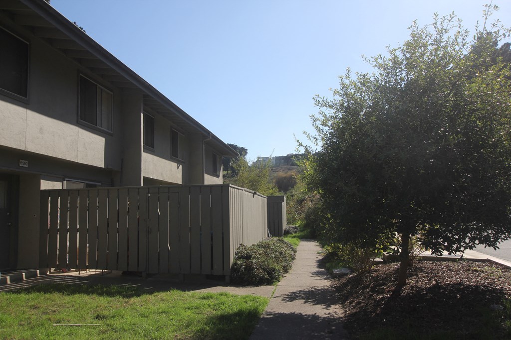 a sidewalk in front of a house with a wooden fence