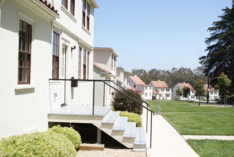 a row of white houses with stairs in front of a lawn and trees