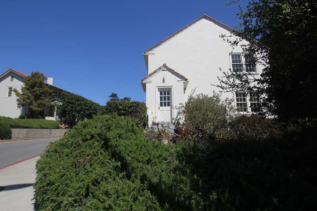 a white house with bushes in front of it on a street