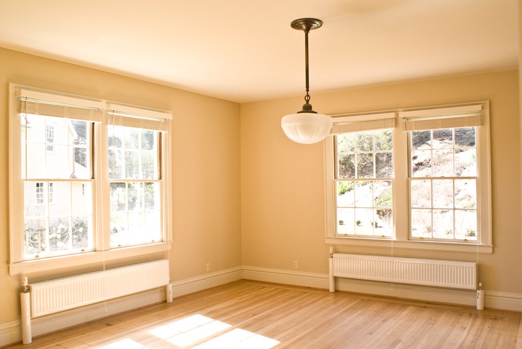 an empty living room with three windows and a pendant light
