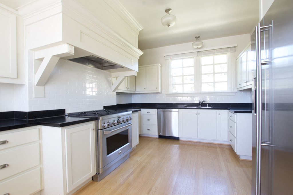 a white kitchen with black counter tops and stainless steel appliances