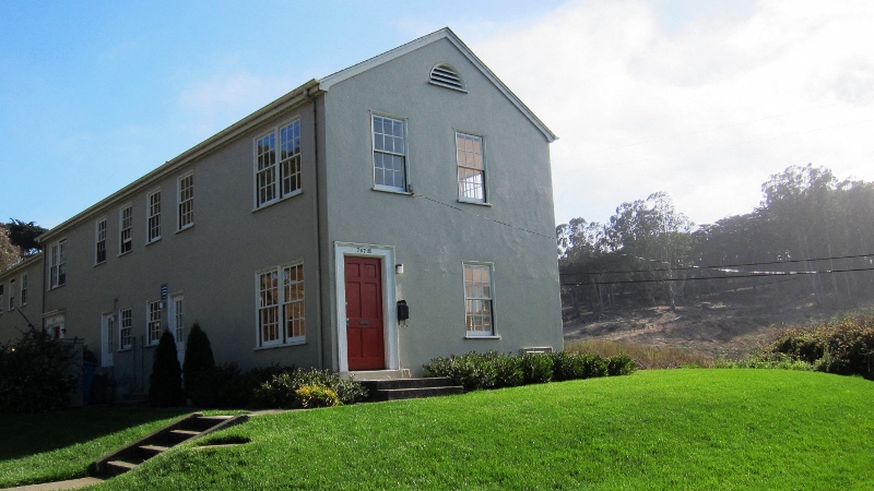 a gray house with a red door on a hill