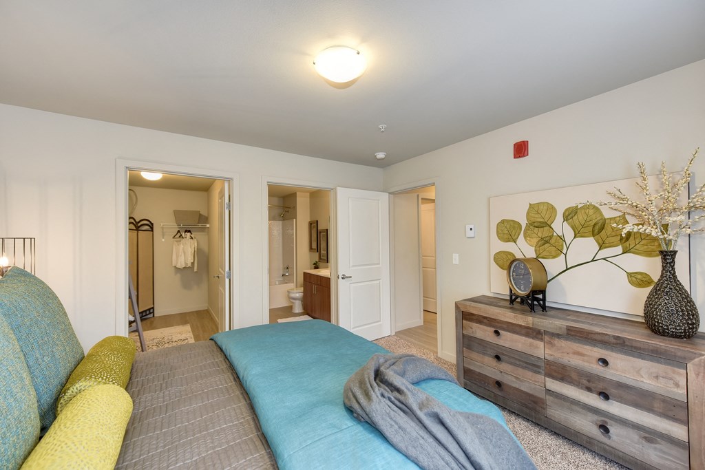 Master Bedroom with Kings Sized Mattress with Blue and Gray Comforter, Carpet, Wood Dressers with Clock and Vase on top, Closet and Bathroom