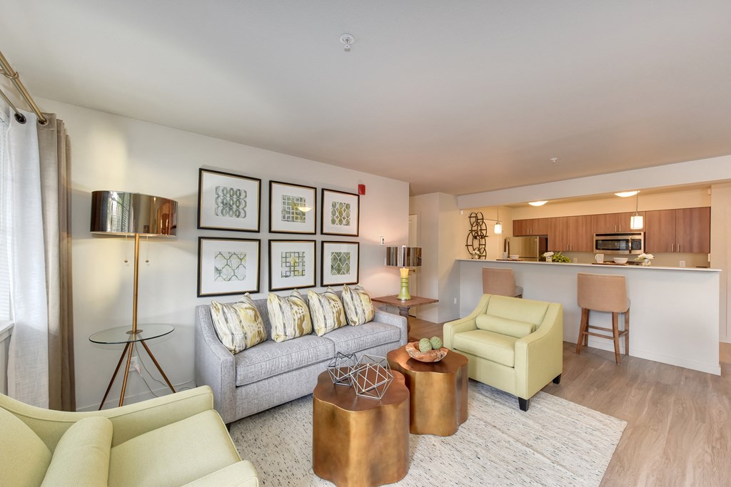 Model Living Room with Couch, View of Kitchen, White Sofa, Hardwood Inspired Floor, Lime Chairs, and Lamp on Glass Table