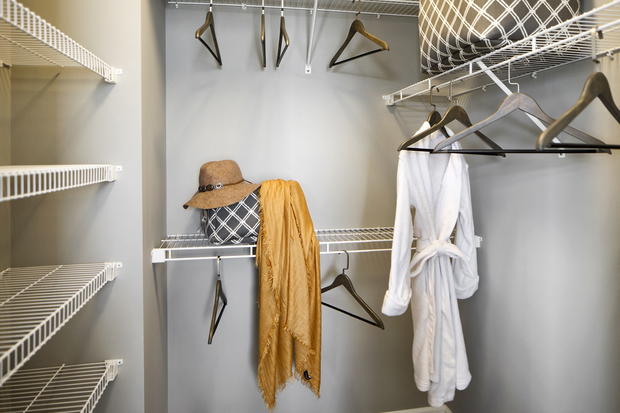 a walk in closet with clothes and a hat on a rack