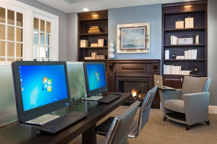 a room with a desk with two computers and a fireplace