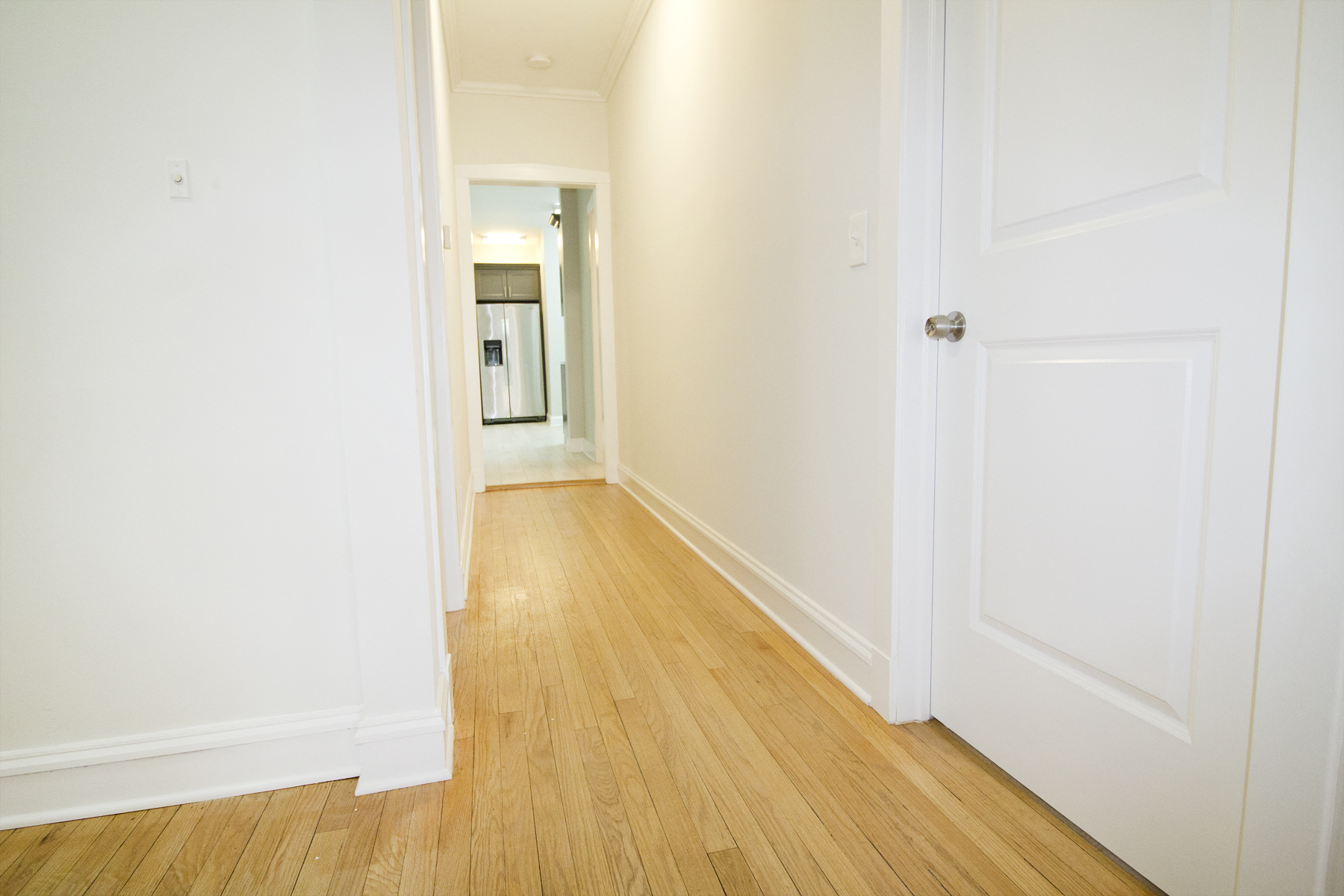 a hallway with white walls and wooden floors and a white door