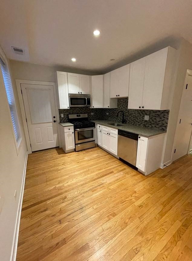 an empty kitchen with white cabinets and a wood floor