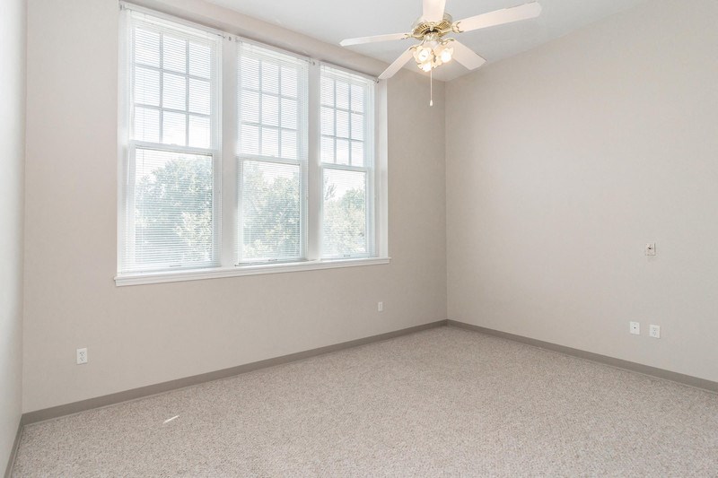 an empty room with three windows and a ceiling fan