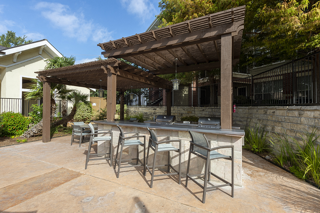 a patio with a bar and chairs under a pergola