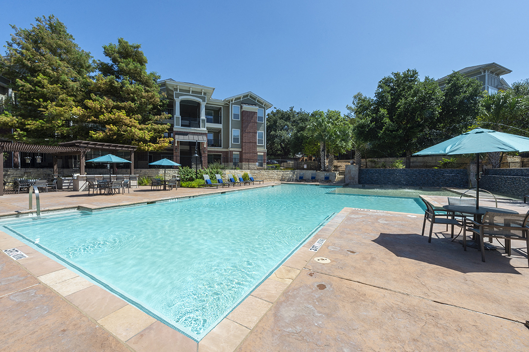a swimming pool with chairs and umbrellas and a building in the background