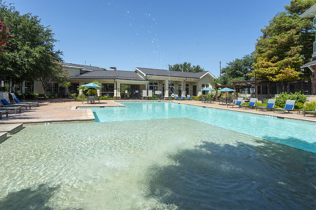 a large swimming pool with chairs and a building in the background