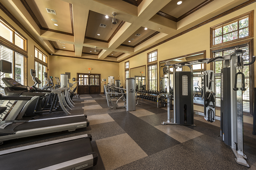 a gym with cardio equipment and weights in a building with windows