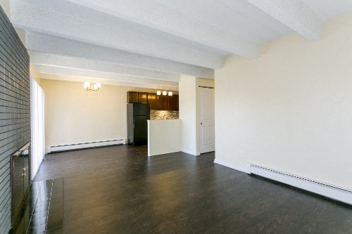 an empty living room with white walls and a black refrigerator