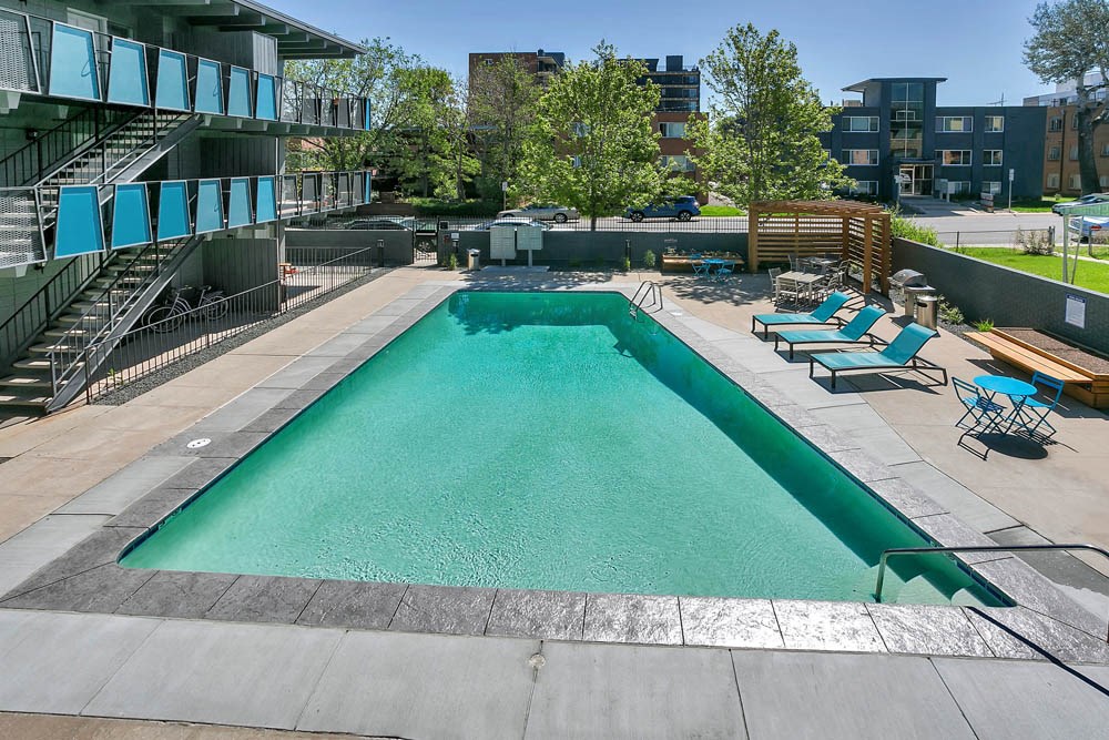 a swimming pool with chairs and a building in the background