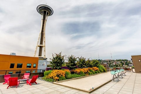 a rooftop patio with red chairs and a view of the space needle in the city
