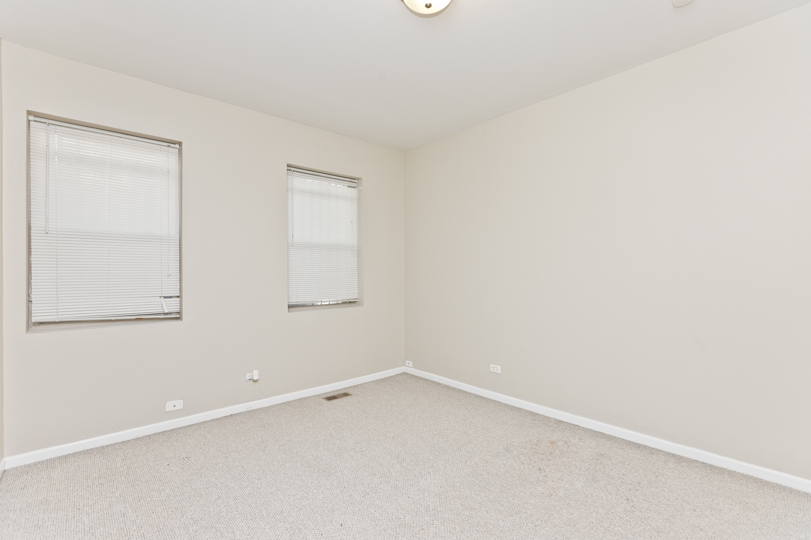 an empty bedroom with two windows and white carpet