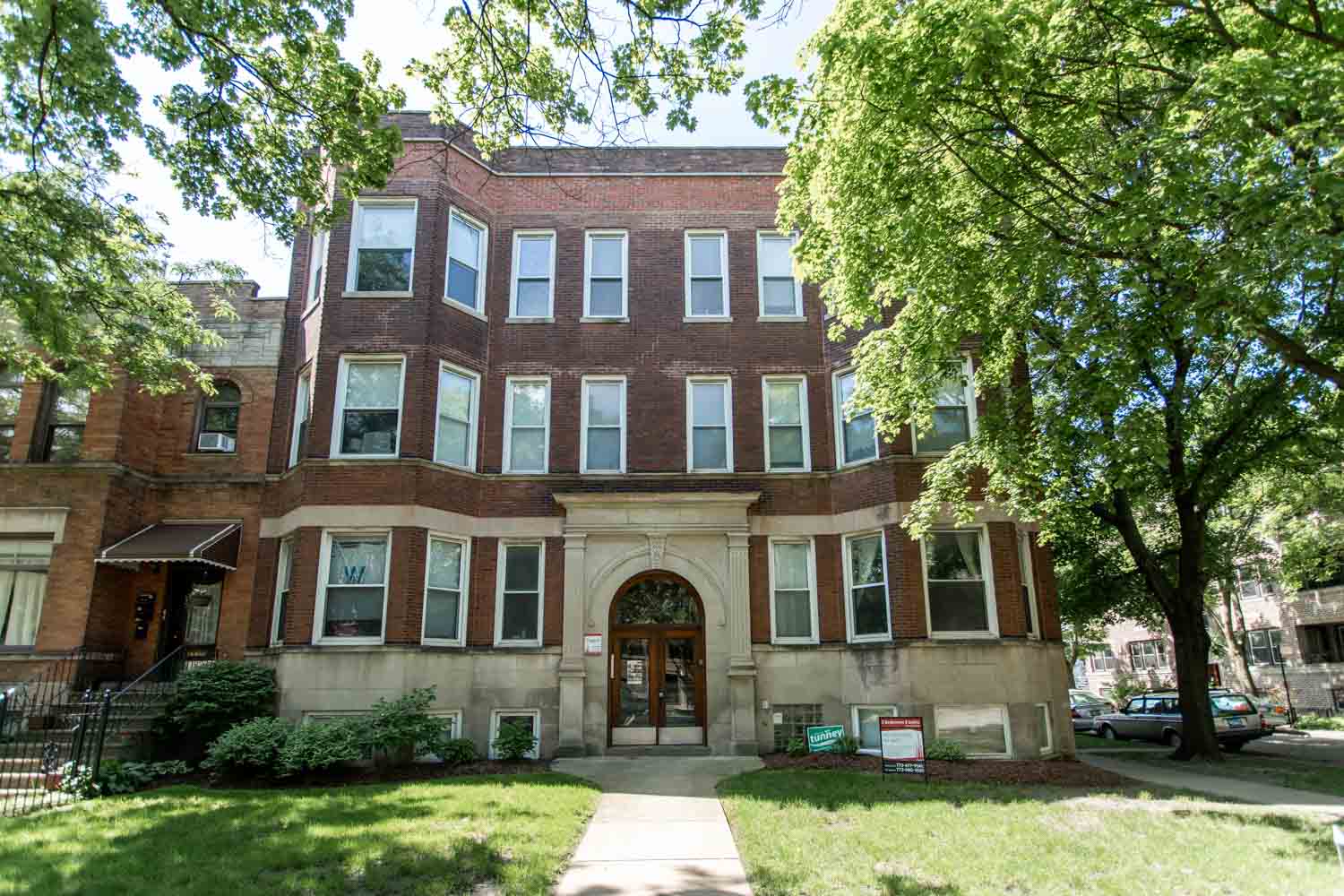 a brick building with a lawn and trees in front of it
