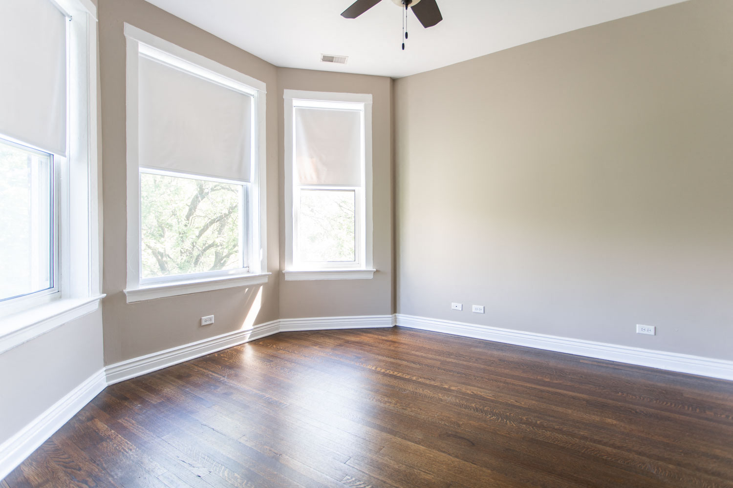 an empty room with wooden floors and three windows