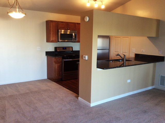 an empty living room with a kitchen with a black counter top