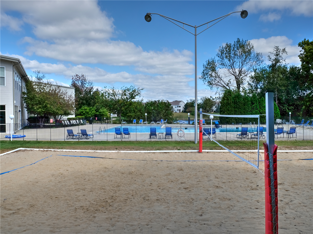 a sand volleyball court in front of a volleyball court and a fence with a pool