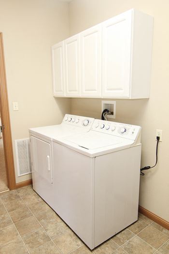 Side by side washer and dryer with storage cabinets above in laundry room