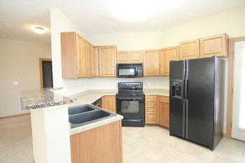 Kitchen with warm brown cabinets, black appliances, and granite breakfast bar.