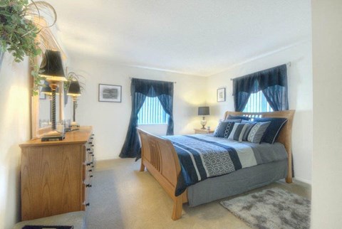 Master bedroom with blue curtains and nightstand lamp at Chili Heights Apartments, New York, 14624